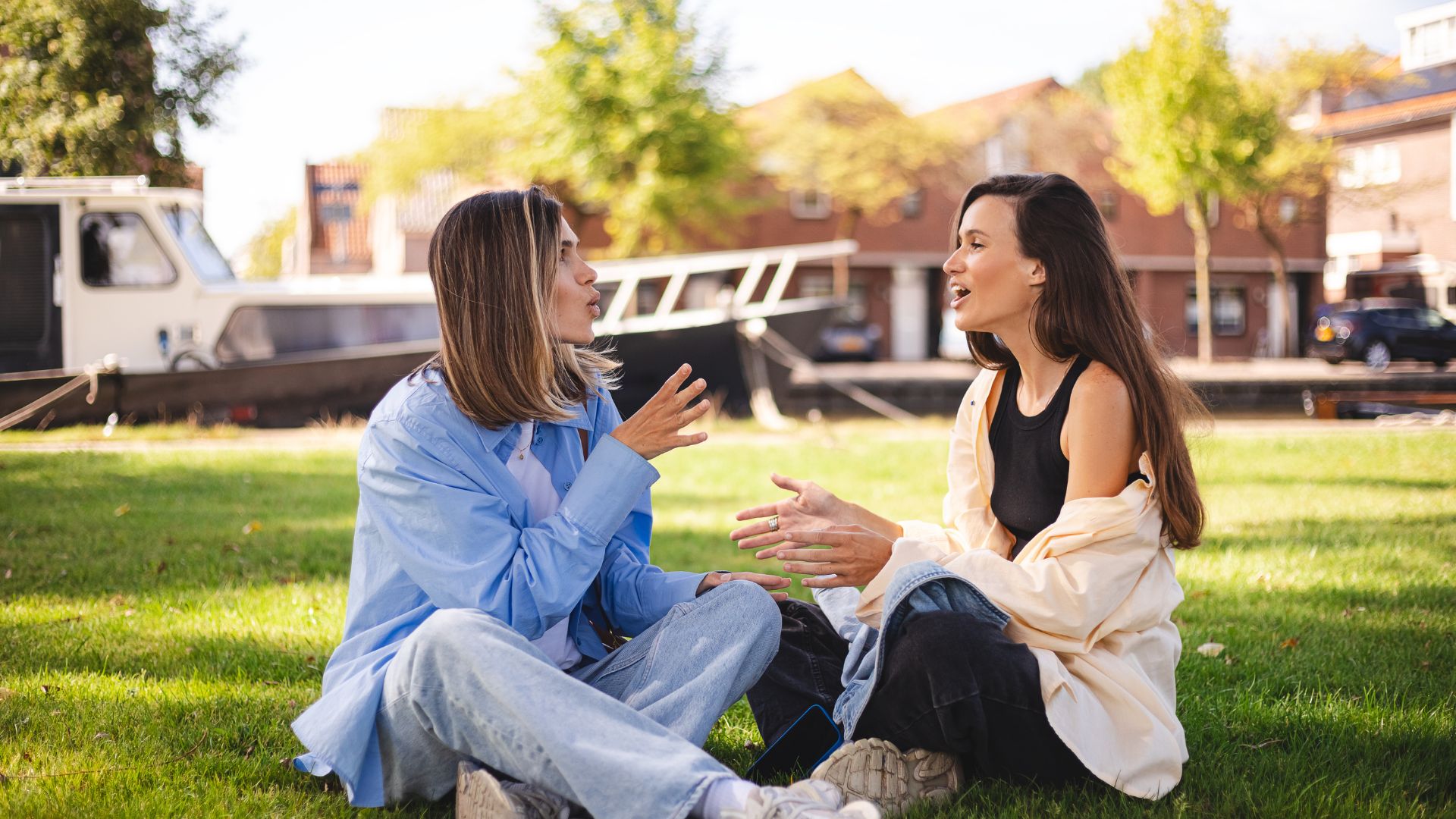 Two women sit on the grass in a park having an engaged conversation, suggesting a thoughtful discussion about future planning and important legal decisions such as a Durable Power of Attorney