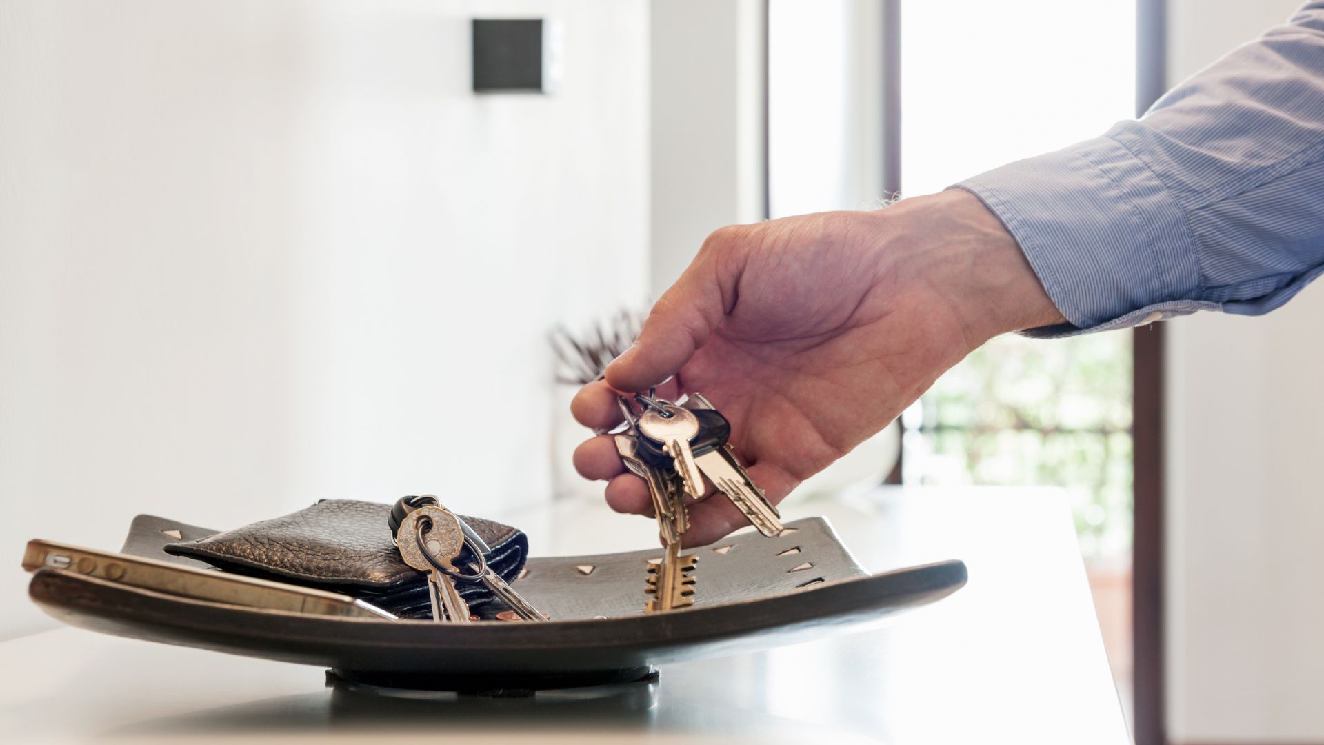 A person’s hand reaches for a set of house keys from a tray that also holds a wallet and phone, symbolizing responsibility and access-possibly representing the authority granted through a Durable Power of Attorney to manage someone else’s property or affairs